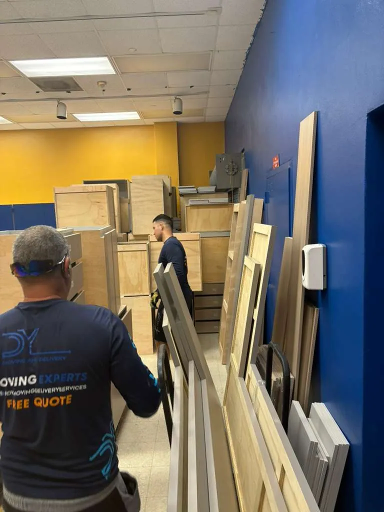 DY Moving mover in company shirt carrying wooden cabinet panels in an office