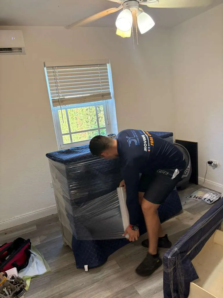 DY Moving mover wrapping furniture in plastic and moving blankets in a bedroom